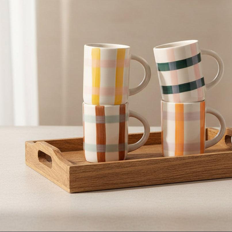 Set of four mugs with colorful striped patterns stacked on a light background