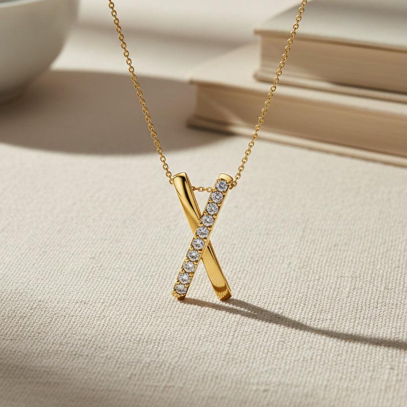 Gold necklace with a 'X' pendant featuring diamonds on a white background