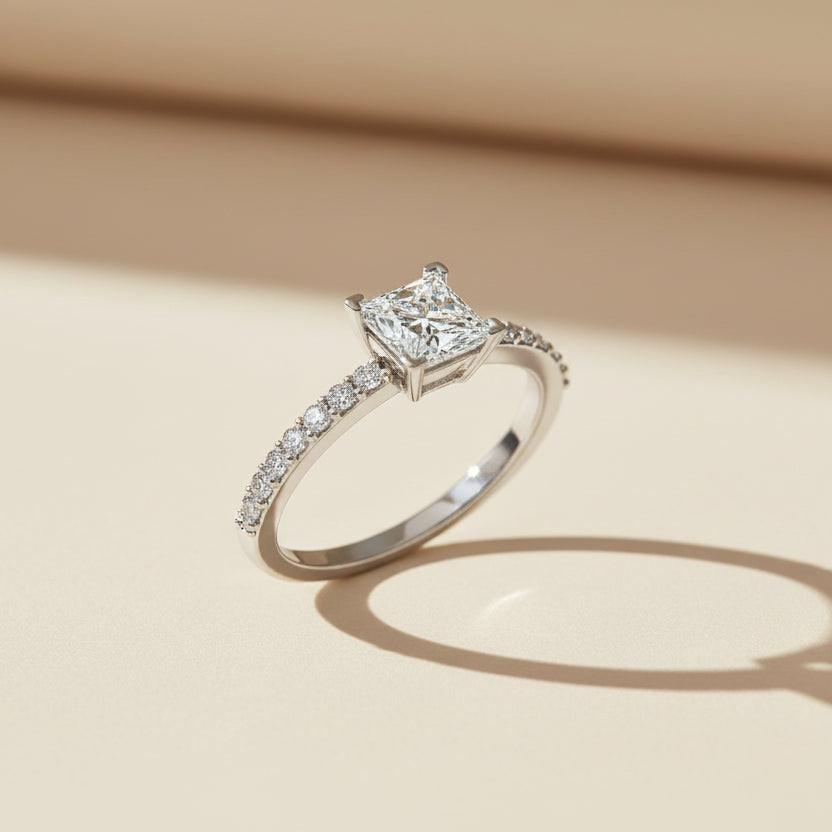 Diamond ring with a central princess-cut diamond and smaller diamonds on the band against a white background