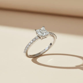 Diamond ring with a central princess-cut diamond and smaller diamonds on the band against a white background