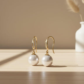 Pearl earrings with gold hooks and diamond accents on a white background