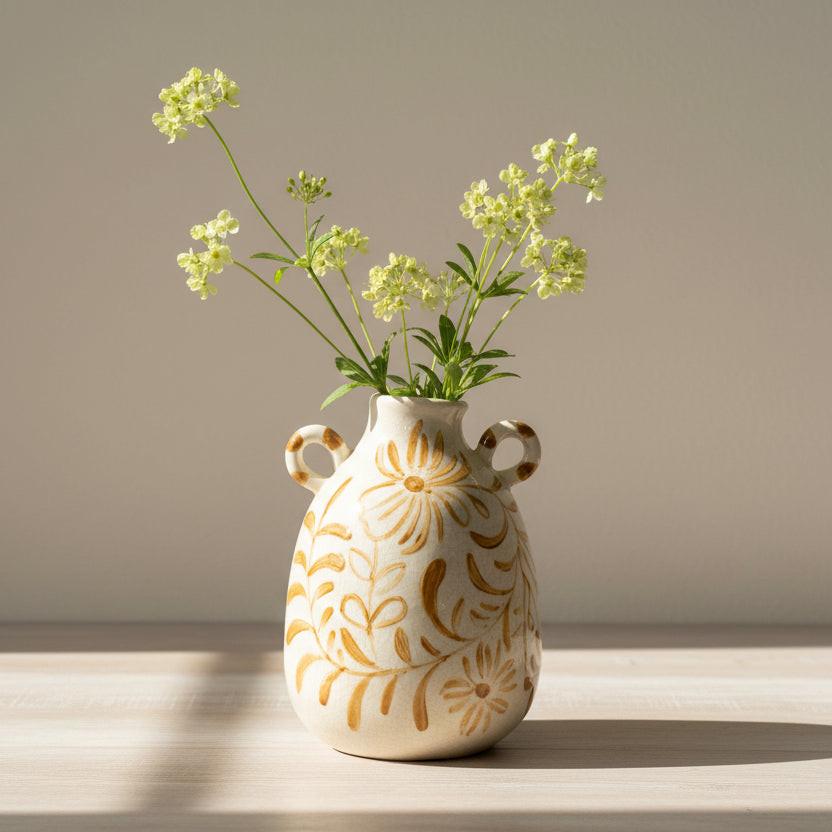 White ceramic vase with gold floral patterns on a wooden surface