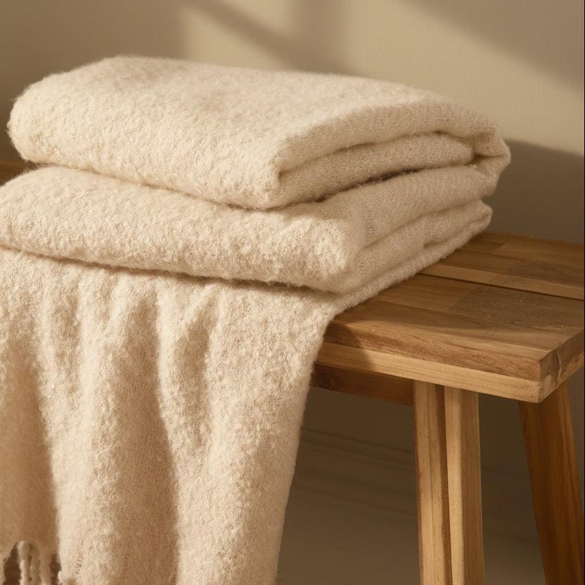 Folded beige blanket with tassels on a wooden table