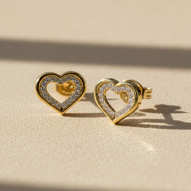Heart-shaped gold earrings with clear gemstones on a white background
