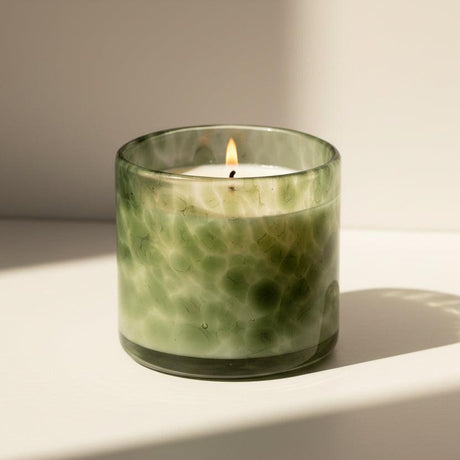 Green glass candle with a lit wick on a white background